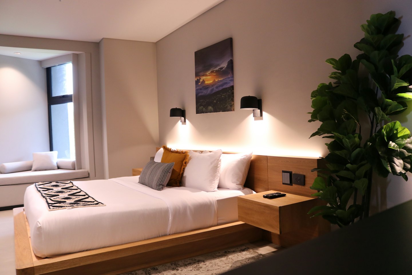 Nowoczesna sypialnia hotelowa z białą pościelą i zieloną rośliną.